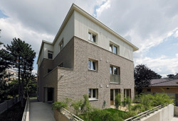 Až nad okna prvního patra vystupuje obklad z lícového zdiva. Nad ním pokračuje světlá omítka ve vertikálním rastru. (Bytový dům s nájemními byty na Barrandově, maak, M.A.Tomáš)