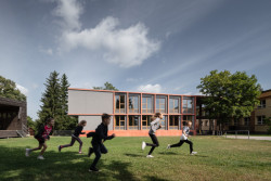 Škola v Podkrkonoší dostala novou přístavbu - s mnoha okny, které vyhlíží do zvlněné krajiny a z probarveného betonu, který připomíná zdejší pískovec (přístavba školy ve Studenci, Chrama, 2021)