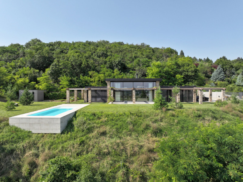 Stavba stojí na svažitém pozemku, má masivní kamenné zdi a vzdušné dřevěné pergoly. (Villa VICUS v Nitře; sebastian nagy architects)