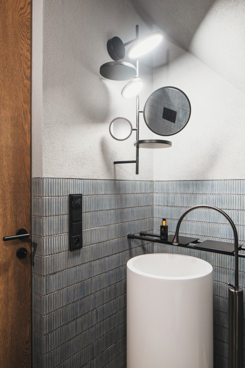 Interiér koupelny pracuje s kontrastem tmavých detailů, strukturovaného obkladu a minimalistického sanitárního vybavení. (Chalupa ve stráni; Mimosa Architekti)