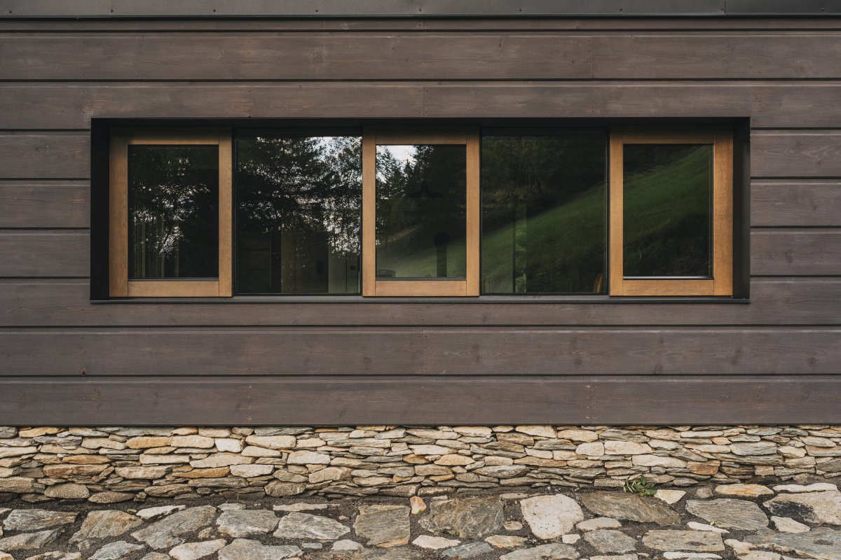 Fasáda pracuje s typickým trojdělením a kamennou podezdívkou, které odkazují na principy tradiční krkonošské architektury. (Chalupa ve stráni; Mimosa Architekti)