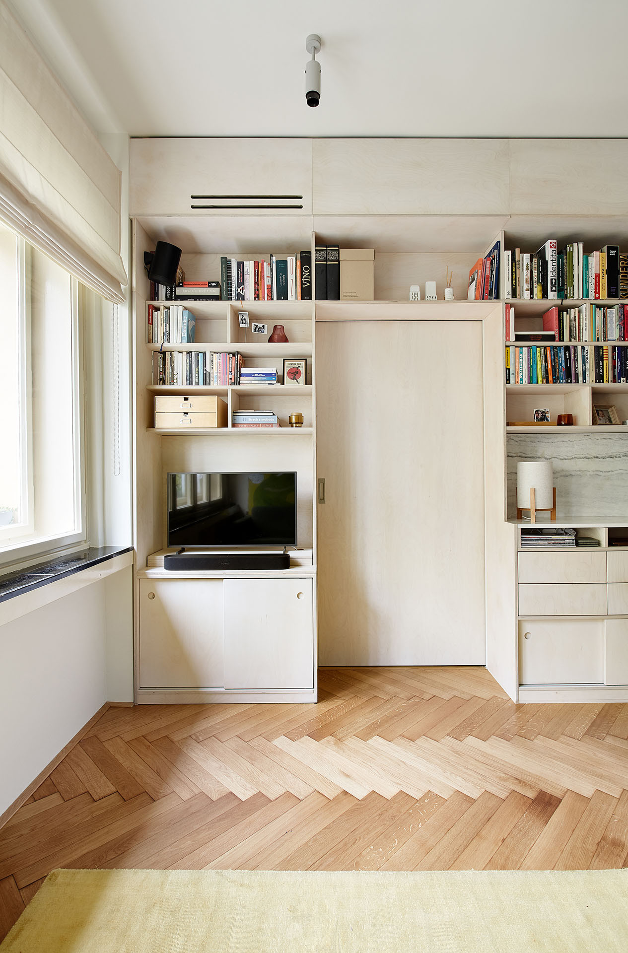 Příčka mezi obytným prostorem a ložnicemi již byla. Architekta do ní pouze navrhla více otvorů, pouzdra posuvných dveři a schovala ji za knihovnu. (Rekonstrukce bytu na Vinohradech, Markéta Bromová architekti)