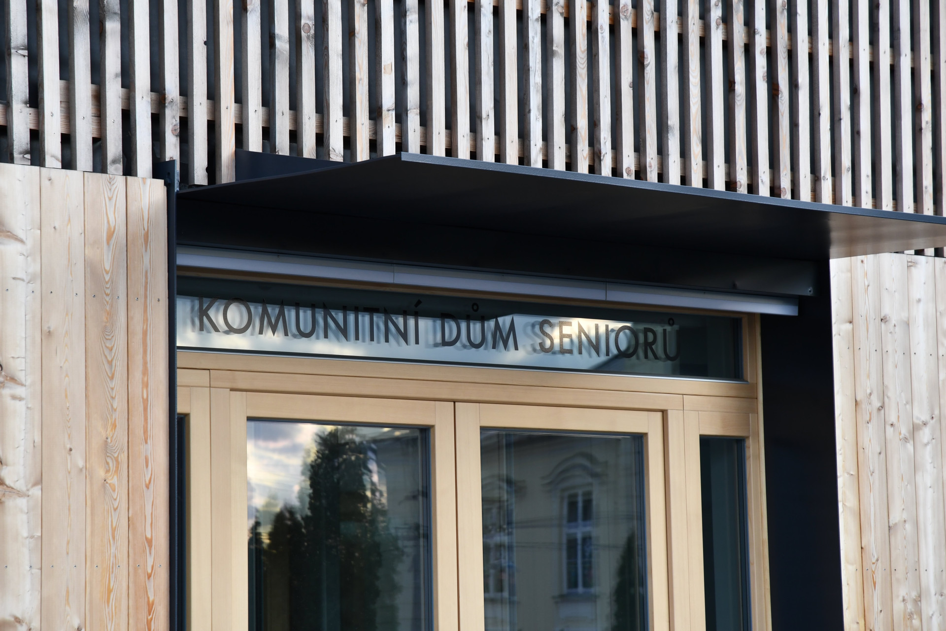 Komunitní dům pro seniory v Holasovicích, City Upgrade: Novostavba je podlouhlá, završuje ji sedlová střecha, fasádní plášť je z modřínových latí