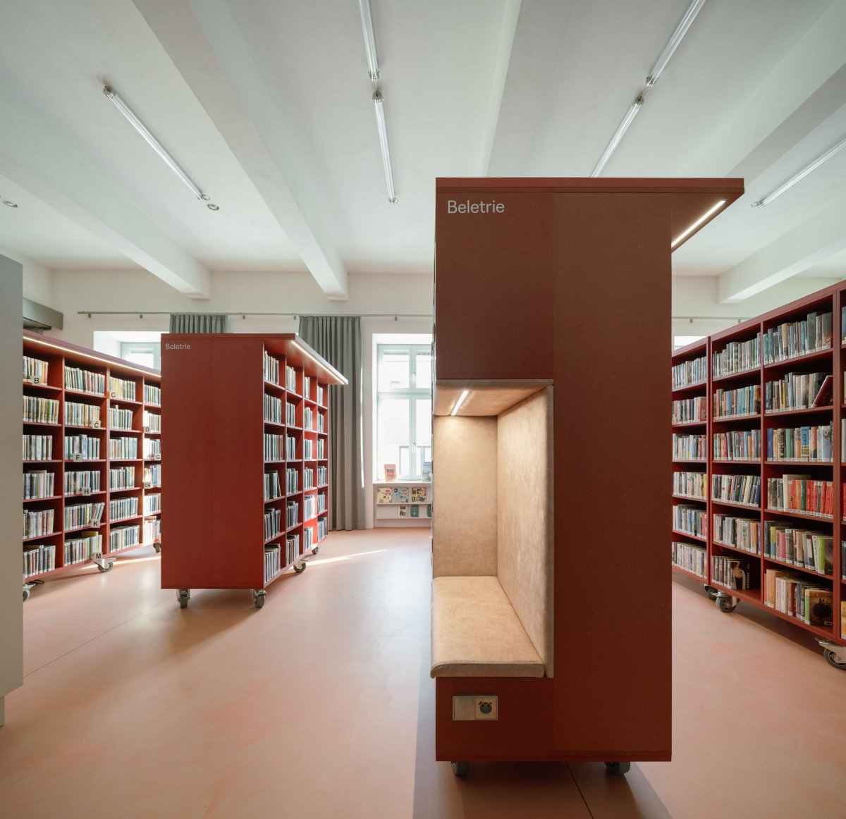 Červeno-růžové regály jsou pak rozmístěné v prostoru. (Knihovna v Červeném Kostelci; Papundekl architekti)
