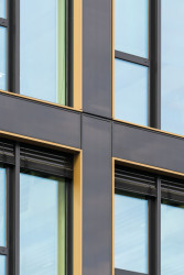 Lemování oken v bronzové barvě vytváří jemný kontrast k téměř černému odstínu fasádních prvků.