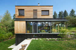 Severní část domu působí, jako by levitovala nad zemí. Celoplošně prosklená zeď v obývacím pokoji rámuje výhled do okolní zeleně. (Chata v Posázaví, Studio Sporadical)