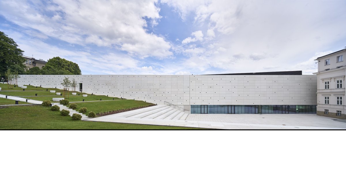 Novostavba má fasádu z betonu, architekti se pro ni inspirovali filmovou páskou. Díky prosklenému parteru působí, jako by se vznášela. (Interaktivním centru pohádek a animace OKO v Bílsko-Bělé v Polsku, Nizio Design International)
