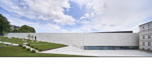 Novostavba má fasádu z betonu, architekti se pro ni inspirovali filmovou páskou. Díky prosklenému parteru působí, jako by se vznášela. (Interaktivním centru pohádek a animace OKO v Bílsko-Bělé v Polsku, Nizio Design International)