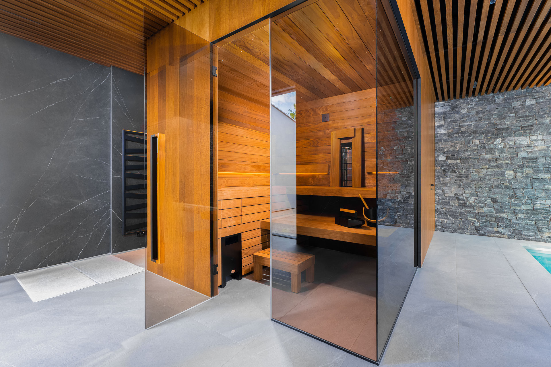 Designová finská sauna TAO v privátním spa disponuje tmavým obkladem, černými doplňky, stěnami zasklenými zatmaveným sklem a zádovým infrapanelem. 