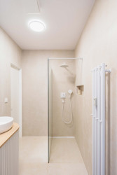 I v koupelně je řada bílých prvků, doplňují je béžové velkoformátové obklady. (Rekonstrukce bytu v Karlíně, Dominik Cvrček)