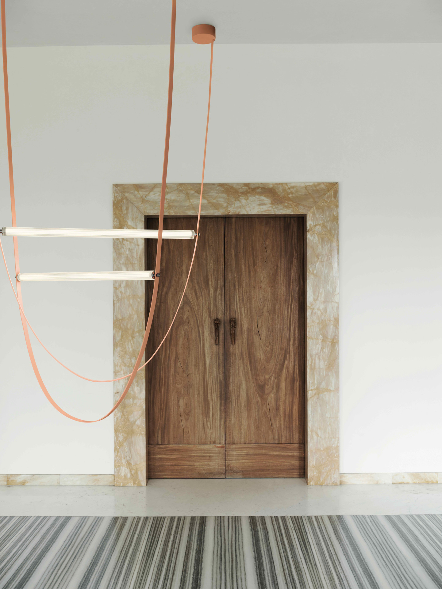 Svítící trubice z bílého mléčného skla a mléčného polykarbonátu disponuje 130 cm dlouhou svítící plochou. Závěs z gumy je variabilní, co se týče délky 65 – 295 cm.