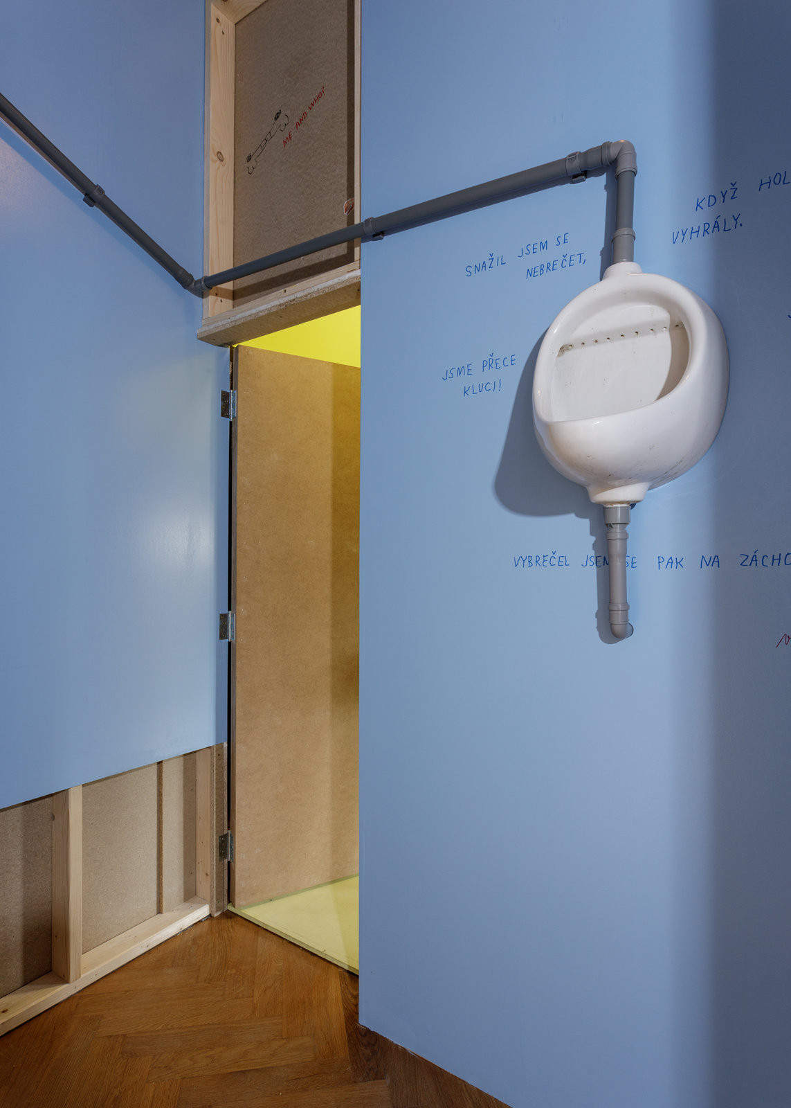 V místnostech jsou na stěnách zavěšené různé předměty, zde pisoár. (Výstava Tělák v Muzeu Prahy)