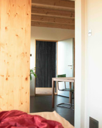 Ložnici vládne červená postel s bavlněným povlečením a bílé zdi. 