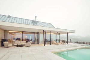 Černé subtilní rámy prosklených exteriérových stěn a černé sloupy dynamicky narušují jednolitost světlých ploch. (Bungalov ve východních Čechách; Atelier Kunc)