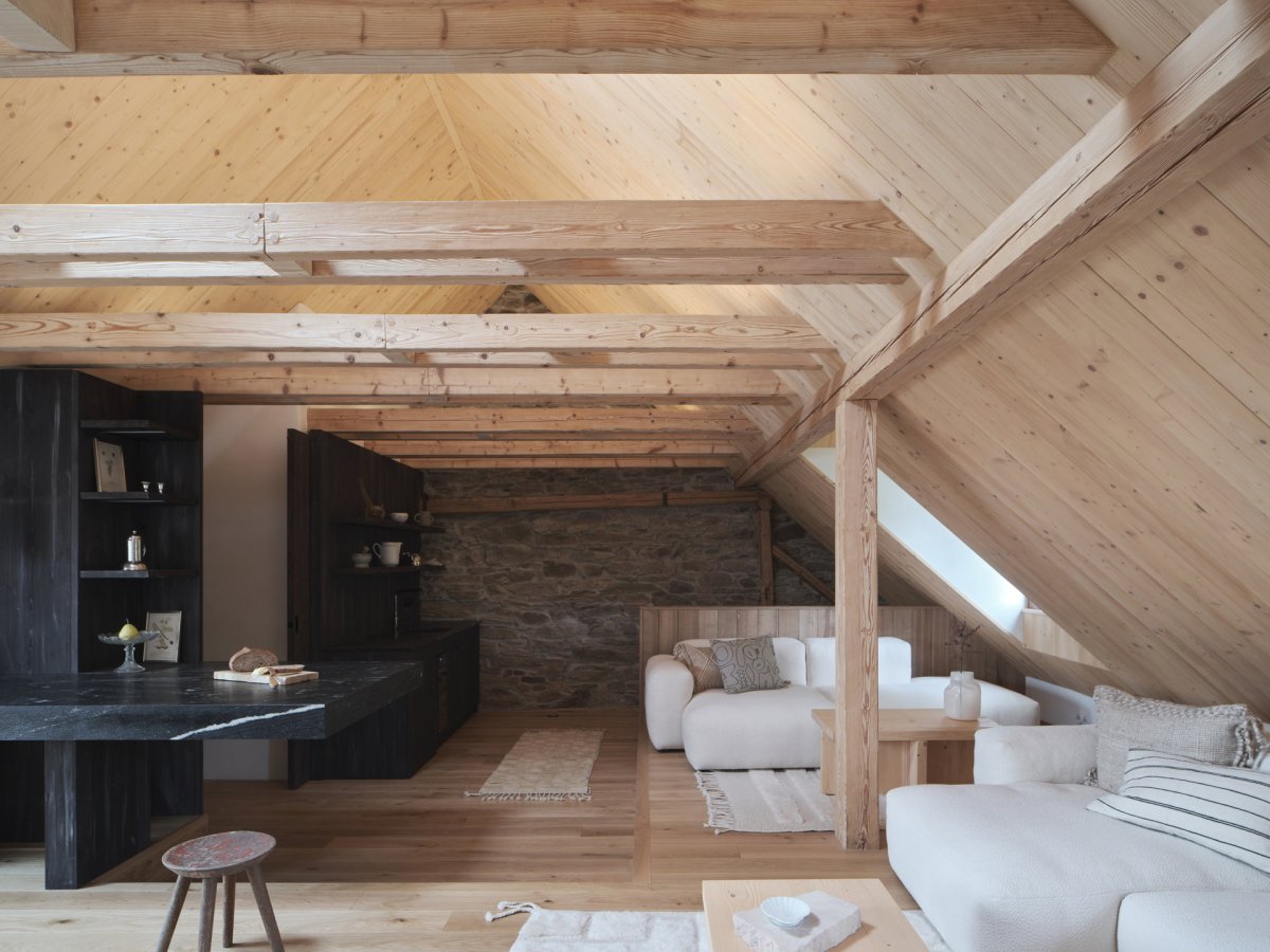 Centrální společenský prostor propojuje původní kamenné konstrukce s masivním smrkovým dřevem a tmavými materiály. (Chalupa na Vysočině; Plus One Architects)