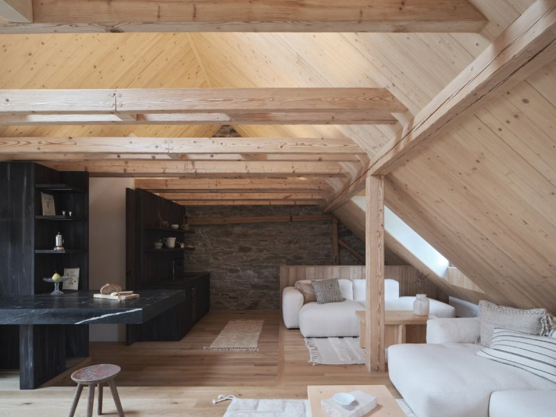 Centrální společenský prostor propojuje původní kamenné konstrukce s masivním smrkovým dřevem a tmavými materiály. (Chalupa na Vysočině; Plus One Architects)